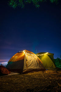 Low angle view of illuminated tent on field against sky at night