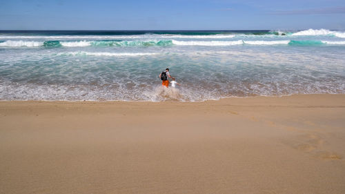 Rear view of man with son enjoying at sea shore against sky