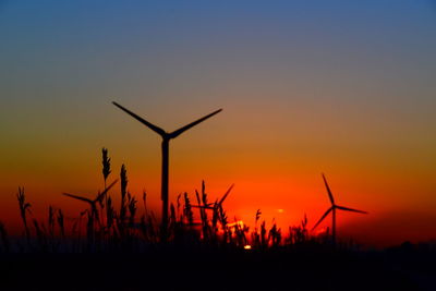 Silhouette wind turbines on field against sky during sunset