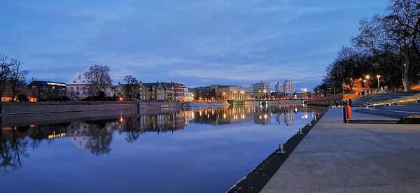 Illuminated city by lake against sky at night