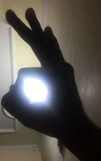 Close-up of silhouette hand on illuminated lamp