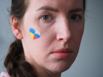 Caucasian woman face flags of russia ukraine painted on cheek shape single heart. no war, democracy