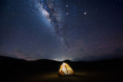 Illuminated tent on landscape against star field at night