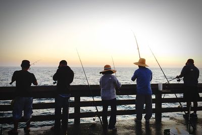 Silhouette people fishing on sea against clear sky