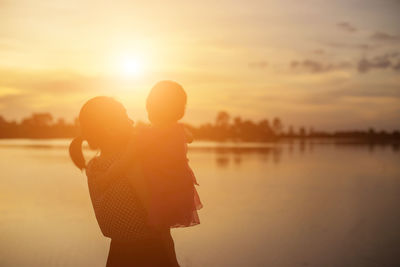 Couple standing by sea against sky during sunset