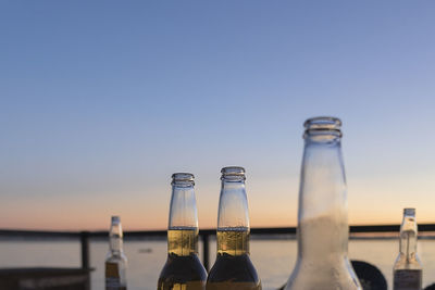 Beer bottles by sea against sky during sunset