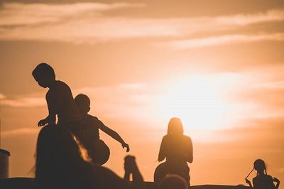 Silhouette people playing guitar against sky during sunset