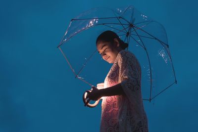 Low angle view of young woman holding umbrella while standing against blue sky at night