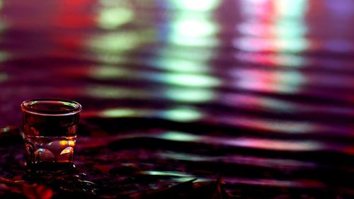 Close-up of beer glass against illuminated water