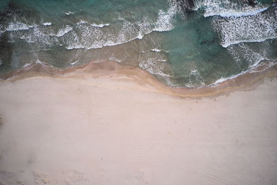 Aerial top view of turquoise water with seaweed and foamy waves rolling on empty sandy beach