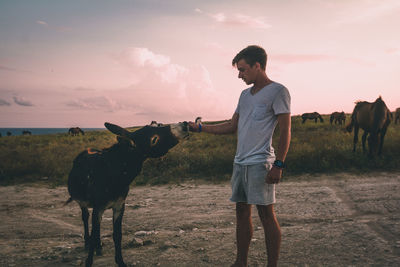 Full length of young woman standing on field against sky during sunset