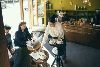 High angle view of barista picking up coffee cups while customers sitting at table