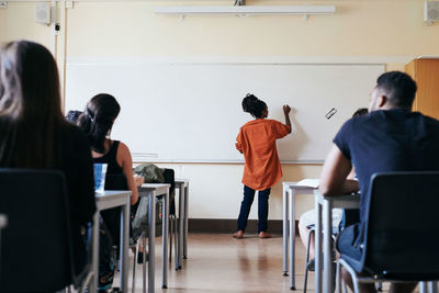 Rear view of female teacher writing on whiteboard in classroom