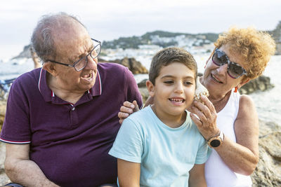 Grandparents and grandson playing with a toy sailboat on the beach