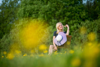 Portrait of young woman with hat sitting on chair at dandelion meadow