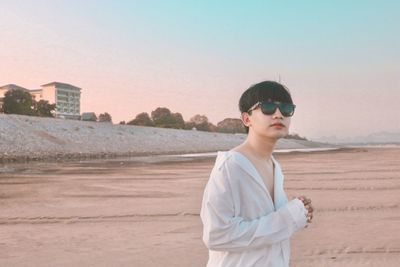 Portrait of man wearing sunglasses while standing on beach against clear sky