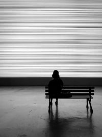 Rear view of person sitting on bench against wall