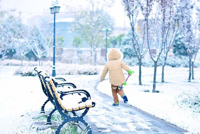 Rear view of child walking by bench on footpath during winter