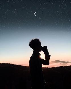 Silhouette boy standing against sky during sunset