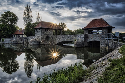 Arch bridge over river by buildings against sky