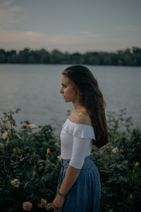 Young woman standing by plants against sky