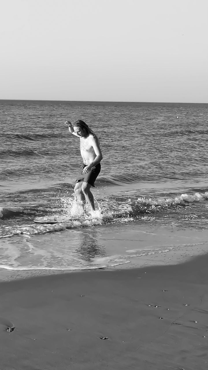 sea, water, horizon over water, horizon, beach, land, sky, motion, one person, wave, nature, white, black and white, beauty in nature, full length, leisure activity, ocean, lifestyles, monochrome photography, day, scenics - nature, men, monochrome, wind wave, holiday, sports, clear sky, coast, black, side view, vacation, surfing, shore, trip, surfing equipment, body of water, sand, outdoors, child, water sports, surfboard, sunny, boardsport, childhood, non-urban scene, tranquility