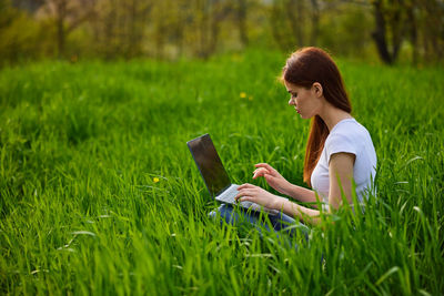 Young woman using mobile phone while sitting on grass