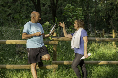 Male mature adult offering water to his workout couple in the middle of the nature in the park