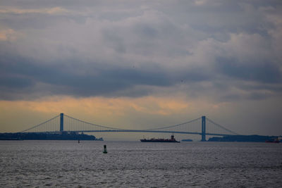 View of suspension bridge over sea against cloudy sky