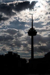 Silhouette of communications tower in city against cloudy sky