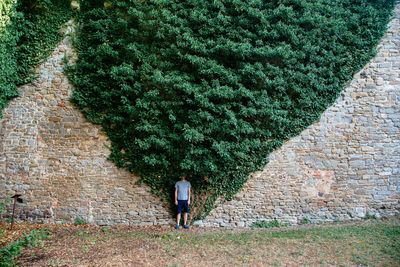 Man standing on field against creeper plants on old wall