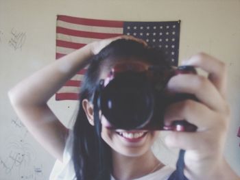 Happy girl holding digital camera in front of american flag