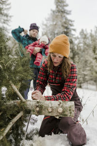 Father carrying daughter while wife cutting pine tree in forest during winter