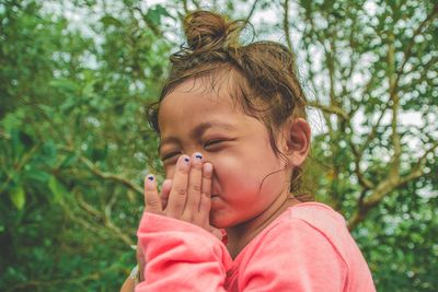 Low angle view of cute girl with eyes closed standing against trees