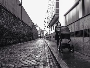 Woman with baby carriage walking in alley at city