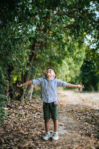 Cute boy standing with arms outstretched against trees