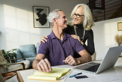 Smiling couple looking each other face to face while using laptop computer at home