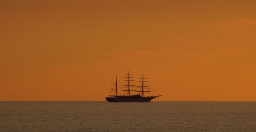 Silhouette ship moored at sea against orange sky