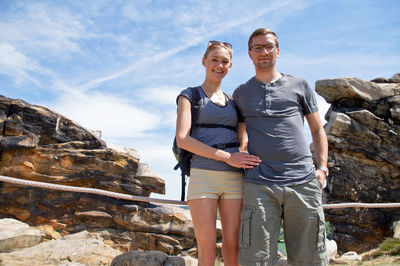 Low angle portrait of smiling young couple standing against sky