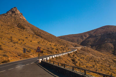 Road leading towards mountain against clear blue sky