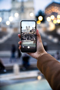 Midsection of person photographing with mobile phone in city