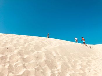 People climbing on sand dune against clear blue sky
