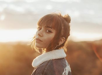 Close-up portrait of young woman standing against cloudy sky during sunset