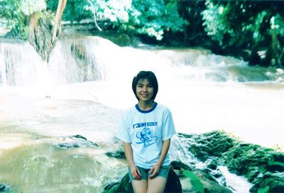 Portrait of young woman standing against waterfall