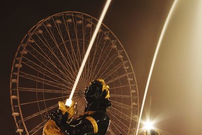 Illuminated statue against ferris wheel at night
