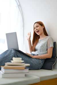 Young woman using mobile phone while sitting on bed at home