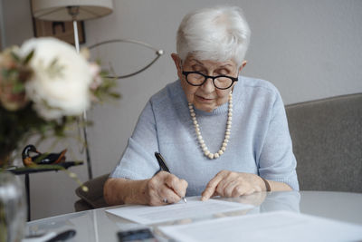 Senior woman writing on paper sitting at home