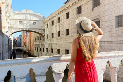 Rear view of young woman wearing hat standing by railing in city