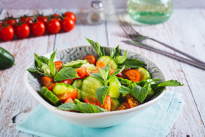 Fresh salad of cucumbers, cherry tomatoes and mint leaves in a bowl on the table