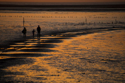 Silhouette people walking on beach against sky during sunset